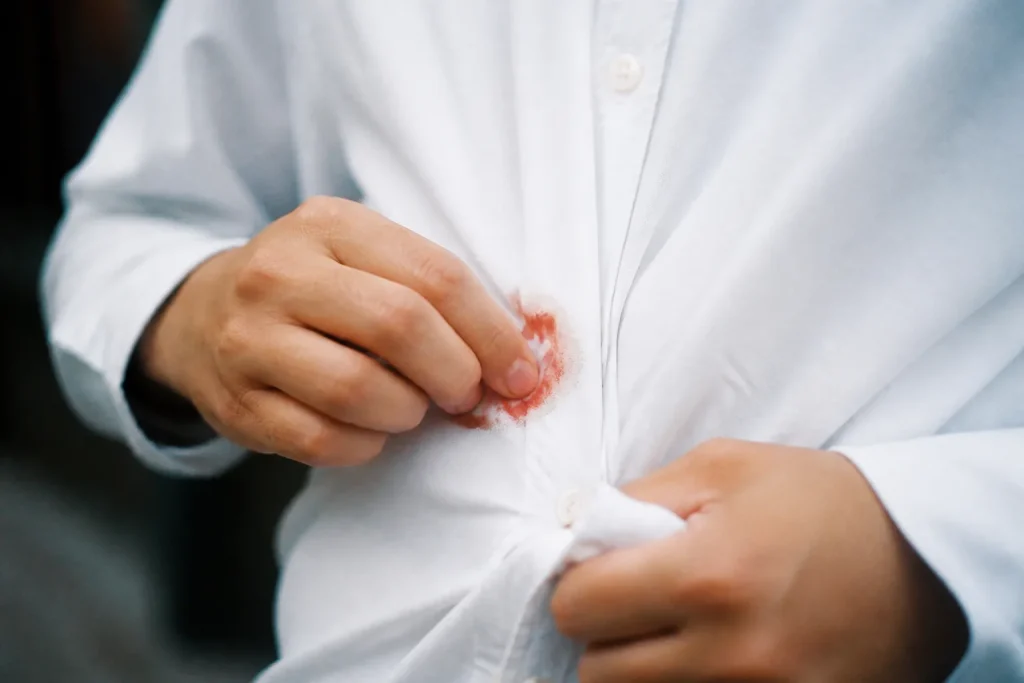 Main frottant une tache rouge sur chemise blanche