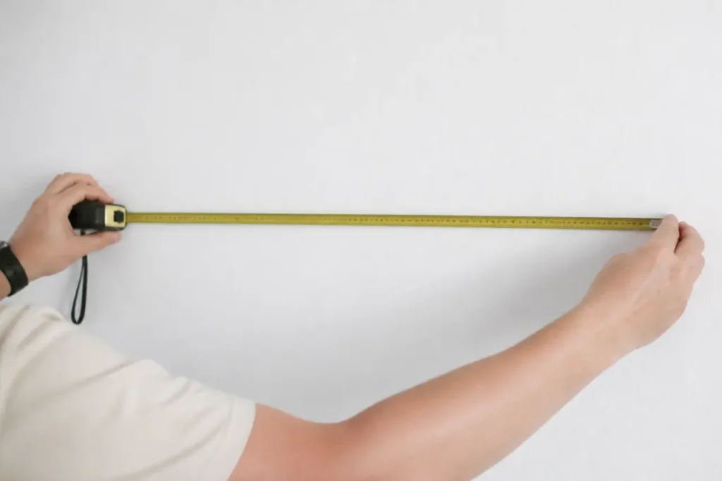 Mains tenant un metre ruban devant un mur blanc